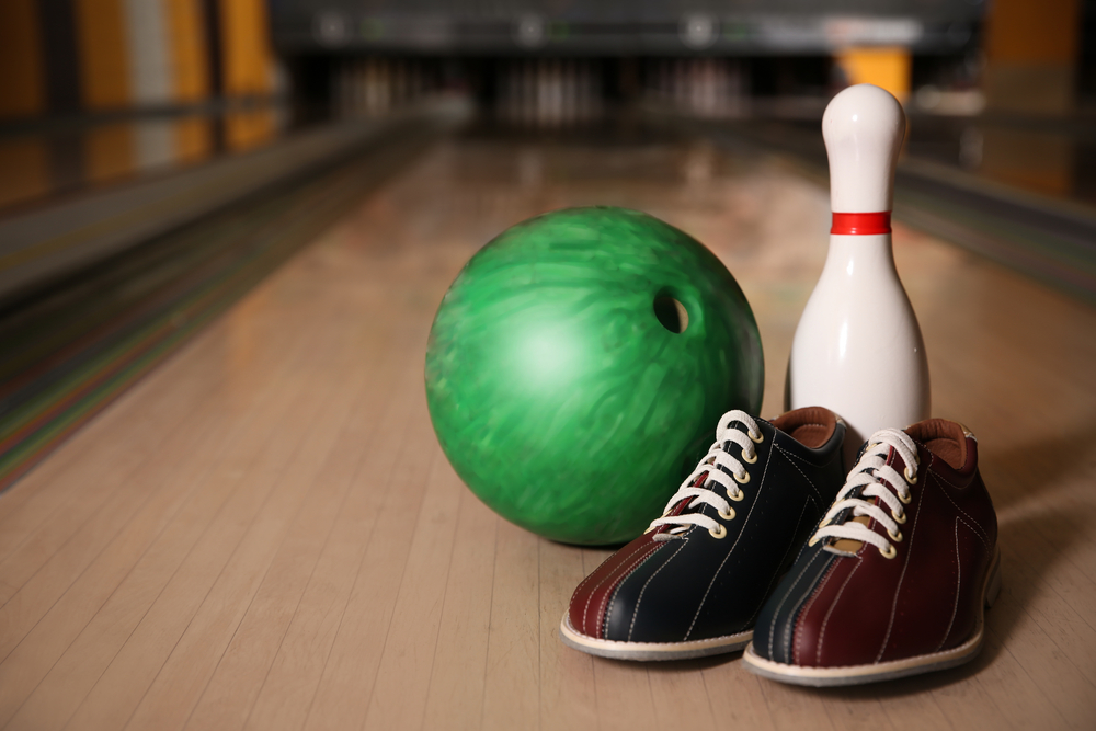 A green bowling ball, ten pin and bowling shoes are on bowling lane.