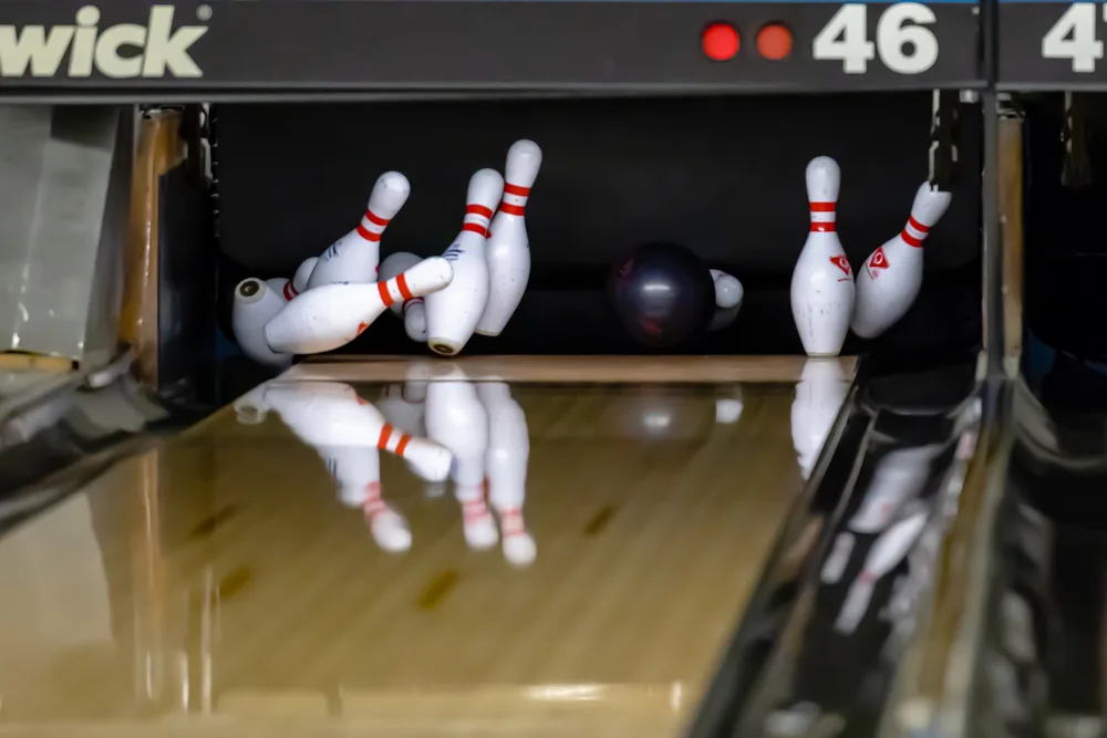 A bowling ball with a light pocket hit at a bowling alley and the black bowling ball at the pin deck