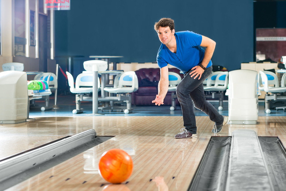 The male bowler in the blue shirt, released the orange bowling ball with his arm pointing straight and just the right amount of speed and arm swings for the strike