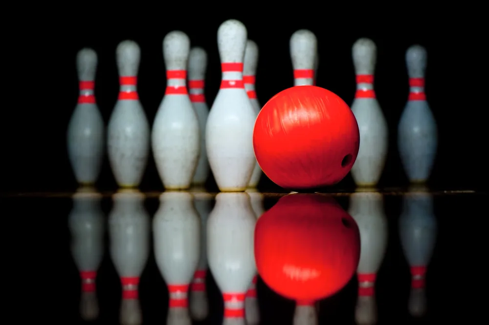 Ten pins with double red bands and red bowling ball are sitting on a bowling lane.