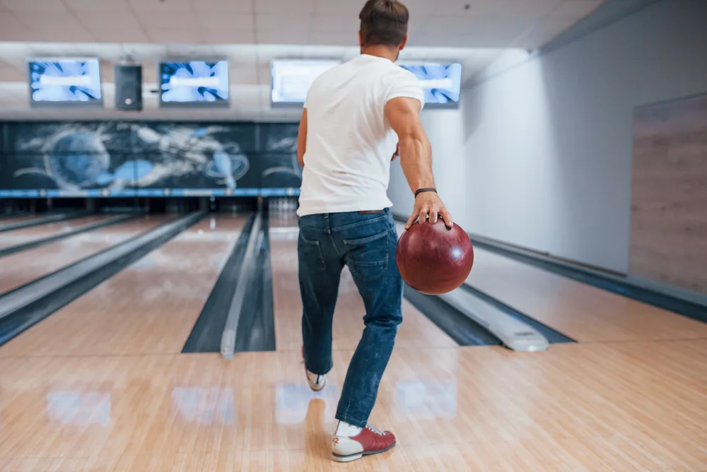 The bowler in the white tshirt rolled the red symmetric ball down the lane.