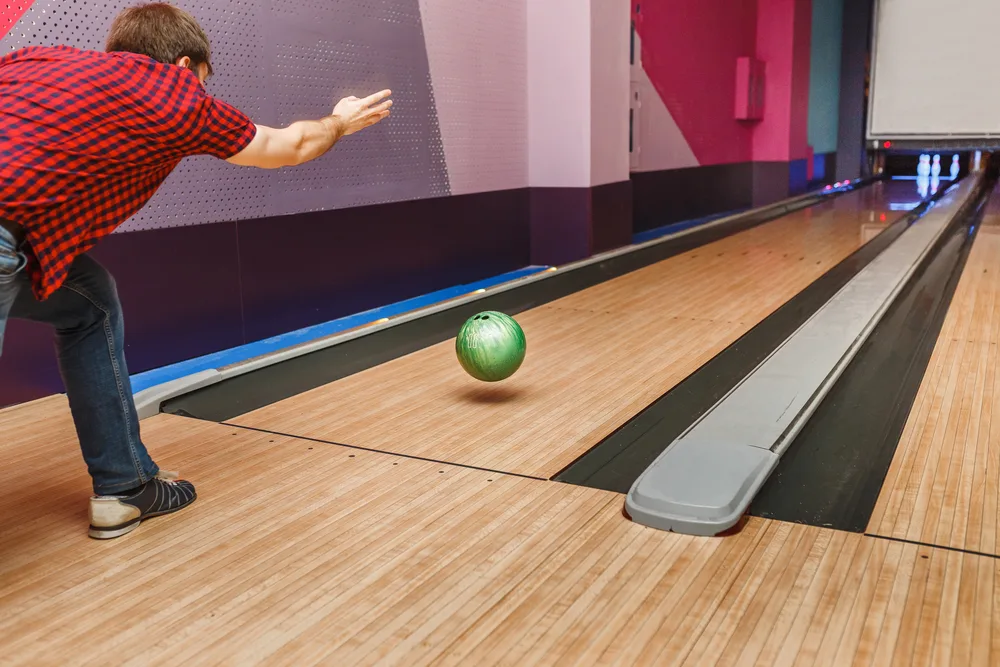 The bowler wears a red shirt and is bowling a red bowling ball and released the ball just in time.