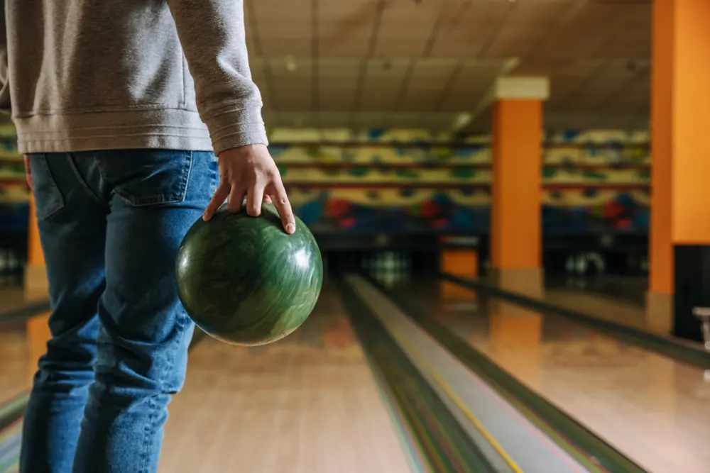 The bowler with the gray sweater and green bowling ball imagines a straight line to the bowling pins.
