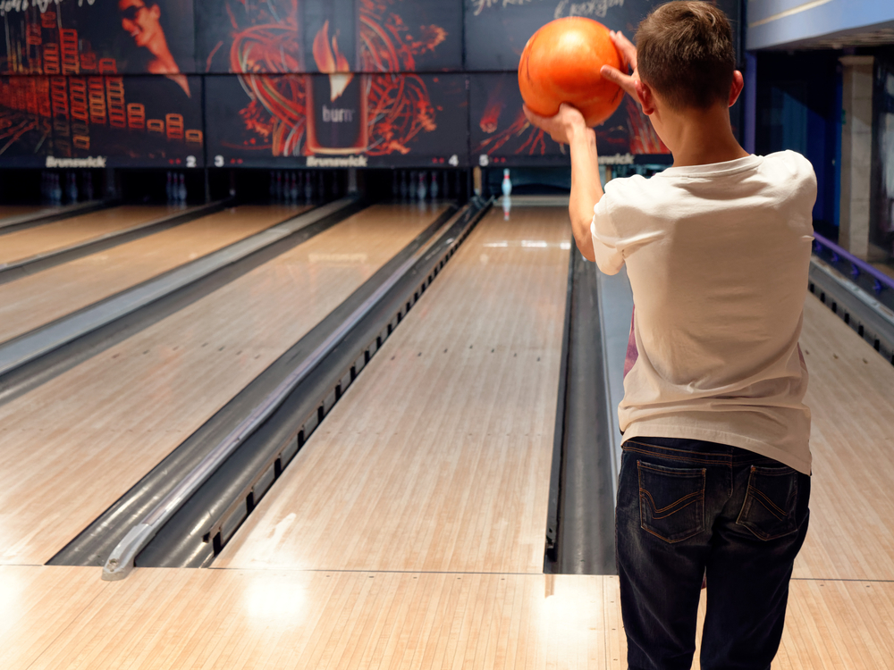 The male bowler in the white tshirt bowling ball deflected off of the first pin and has one pin remaining.