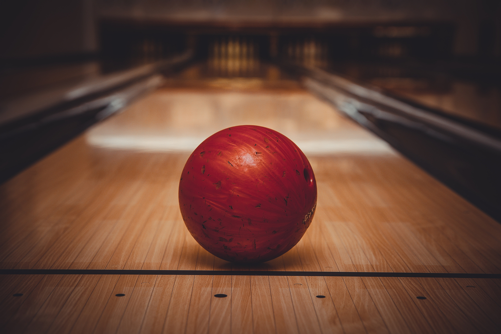 Bowling lane with a red bowling ball at the foul line is the typically synthetic lanes used by both pro and amateurs bowling,