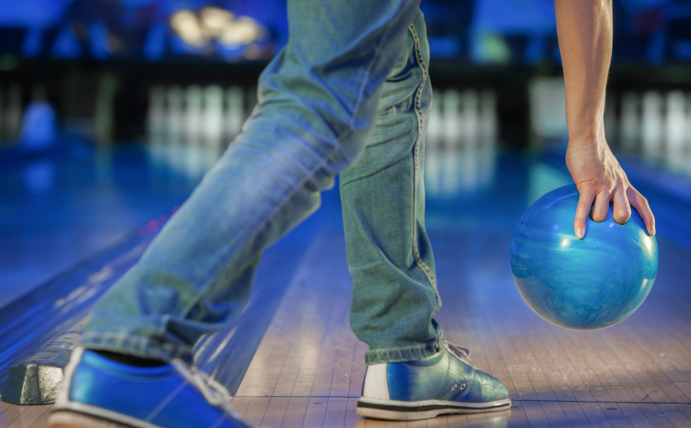 A bowler throwing the blue bowling ball with too much force on the bowling lane.