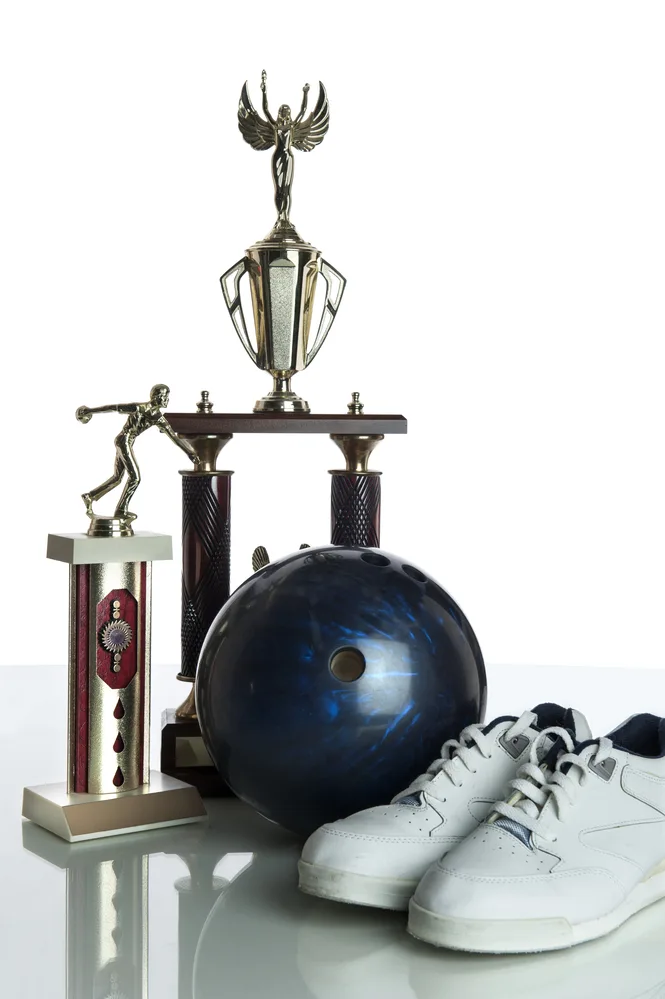 Bowling ball, bowling shoes and trophies on a white background on a table.