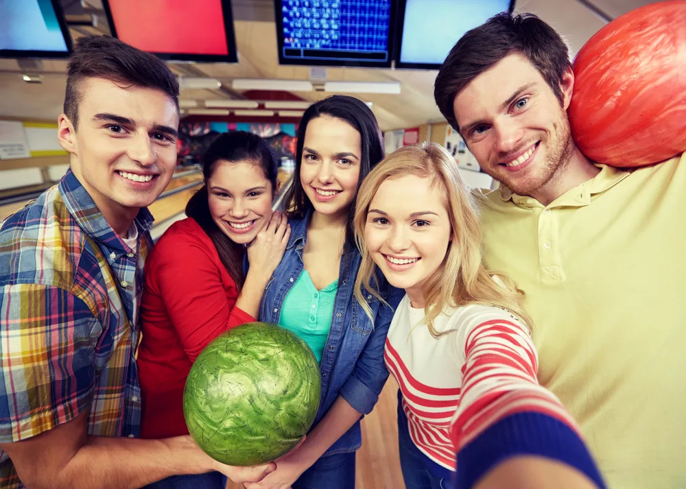 Coworkers taking selfie with in bowling alley holding bowling balls.