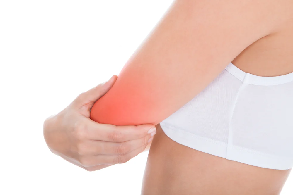 A bowler in a white tank is experiencing pain in her bowling arm.