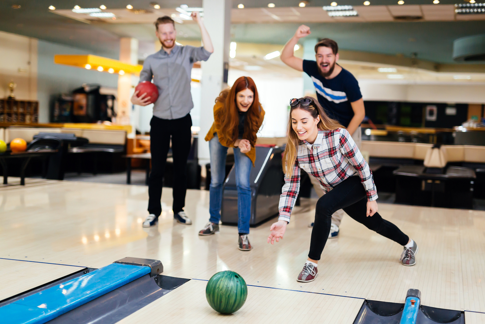 The girl in the plaid shirt is a right handed bowler because she released the green bowling ball from her right hand.