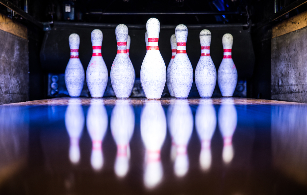 Ten pins are on the lane at a bowling alley, the bowler bowled two bowling balls for a strike.