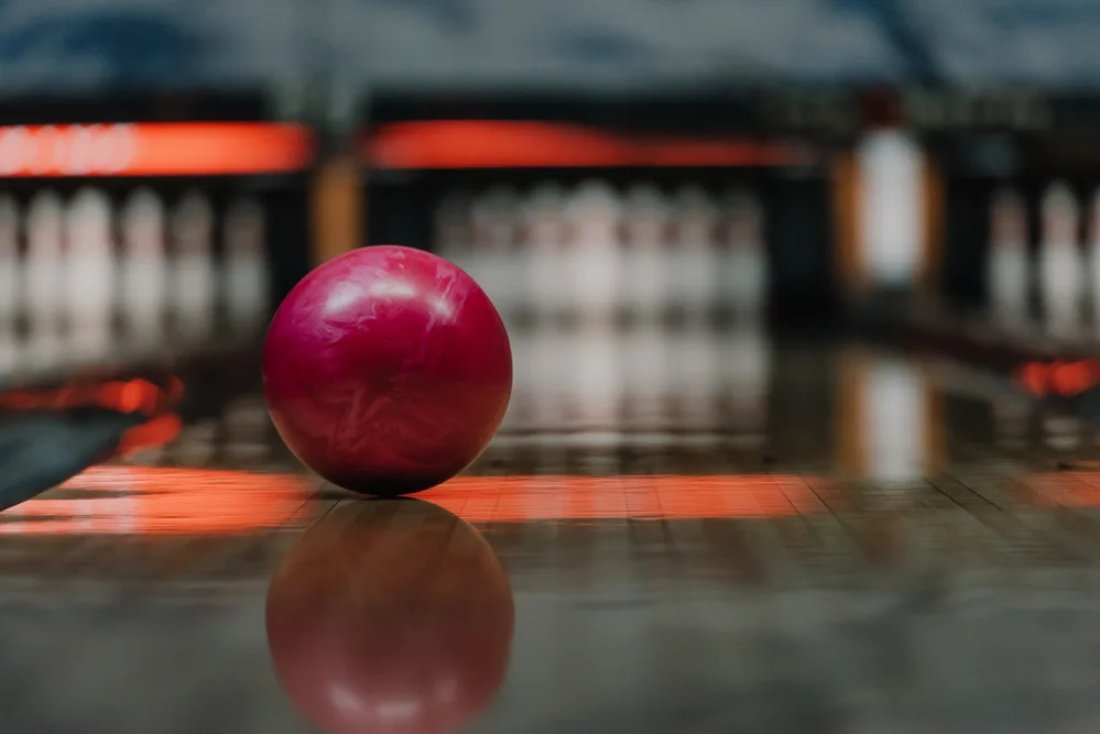 Red bowling ball sitting on the lane has visibly track area on the ball