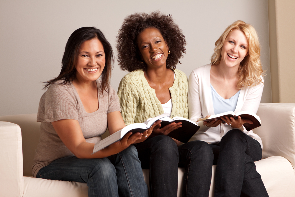 Three bowling ladies sit on a couch reading books to increase their bowling skill levels