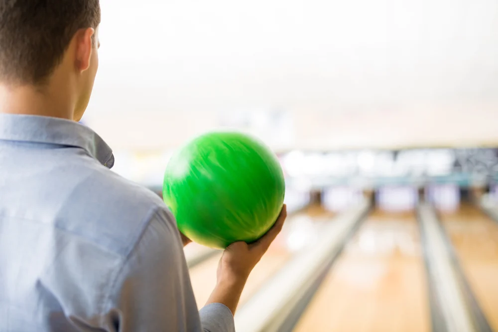 Rear view of teenager playing with green bowling ball in a bowling alley, decided to practice and log is progress.