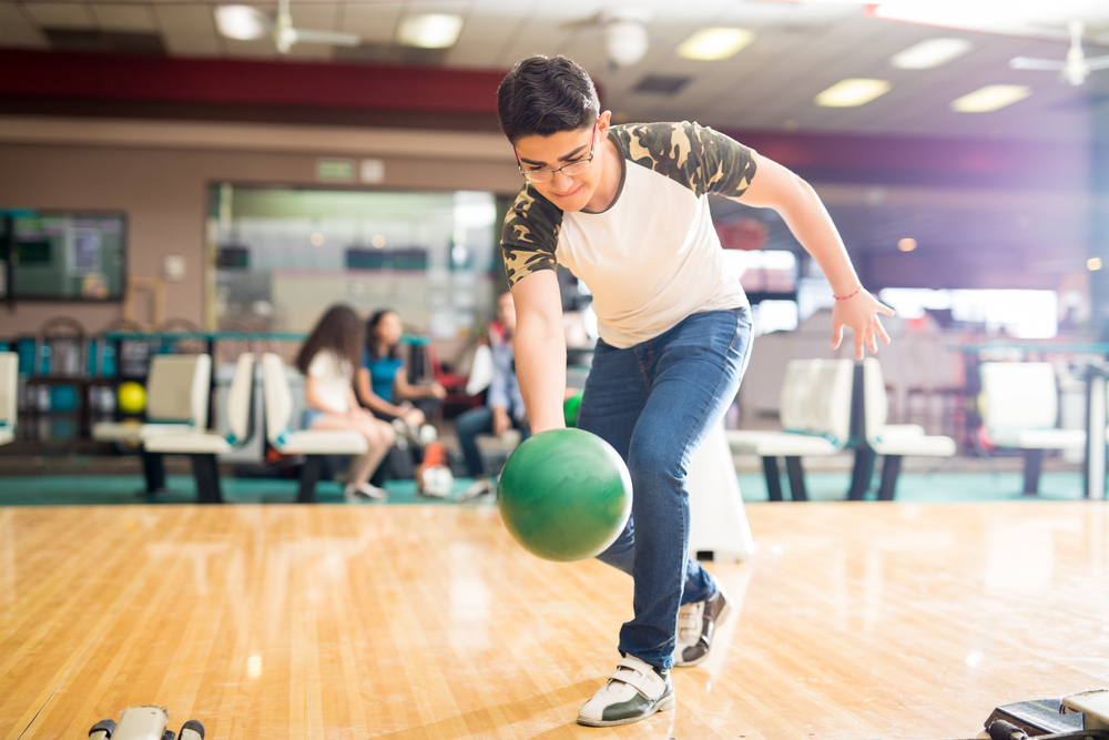 Full length of confident teenage boy practicing his swing at a bowling alley on montreal oil pattern