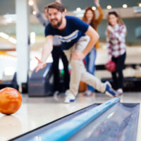 male bowler in blue shirt rolling an orage ball asked his friends what's the perfect score in bowling