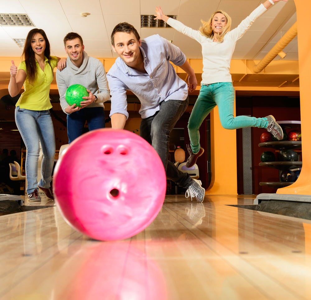 Group of four young smiling people playing bowling trying to avoid a gutter ball