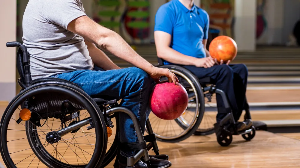 Two bowlers in wheelchairs are sitting at teh foul line, joined a bowling team because they love the natural competition of the sport