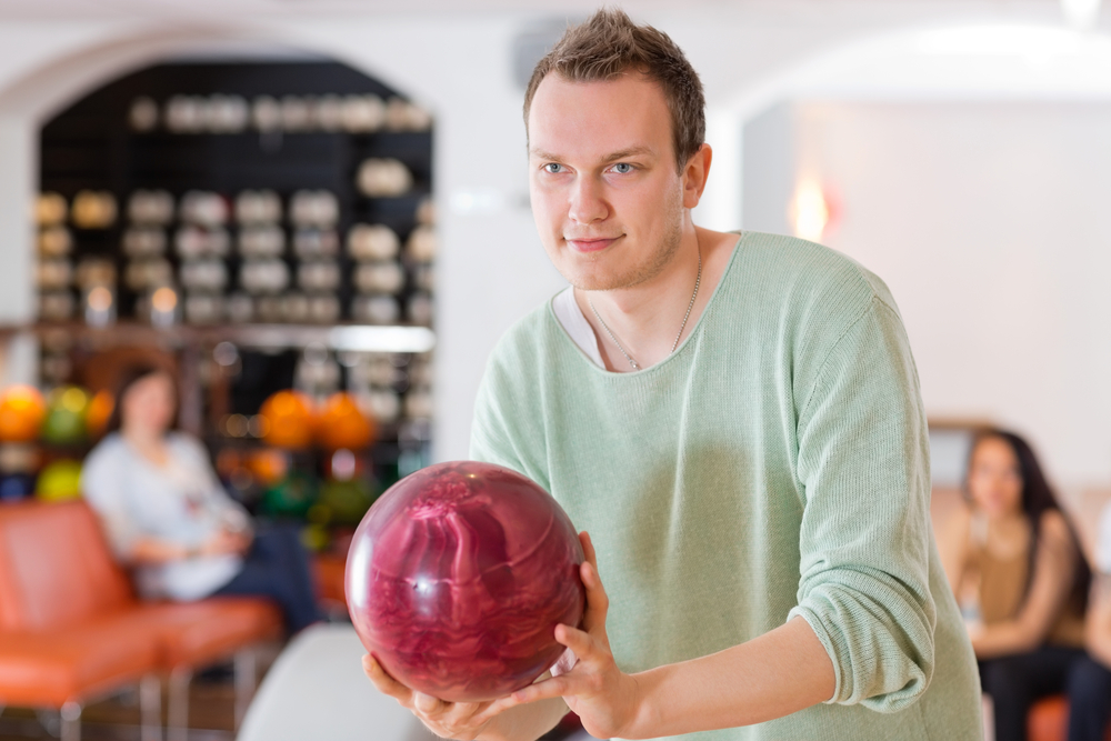 Male bowler in an alley is looking at the lane and realized the oil is there to protect the lane.