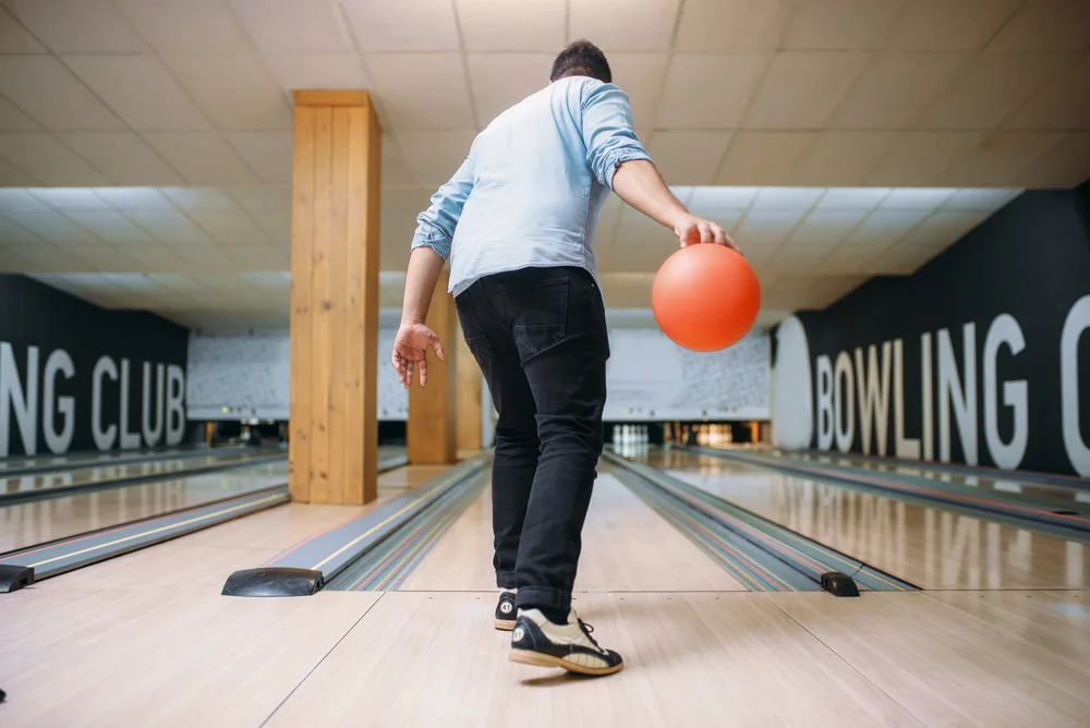 Male bowler standing on lane and poses with ball in hands, back view trying to determine where to throw the ball.