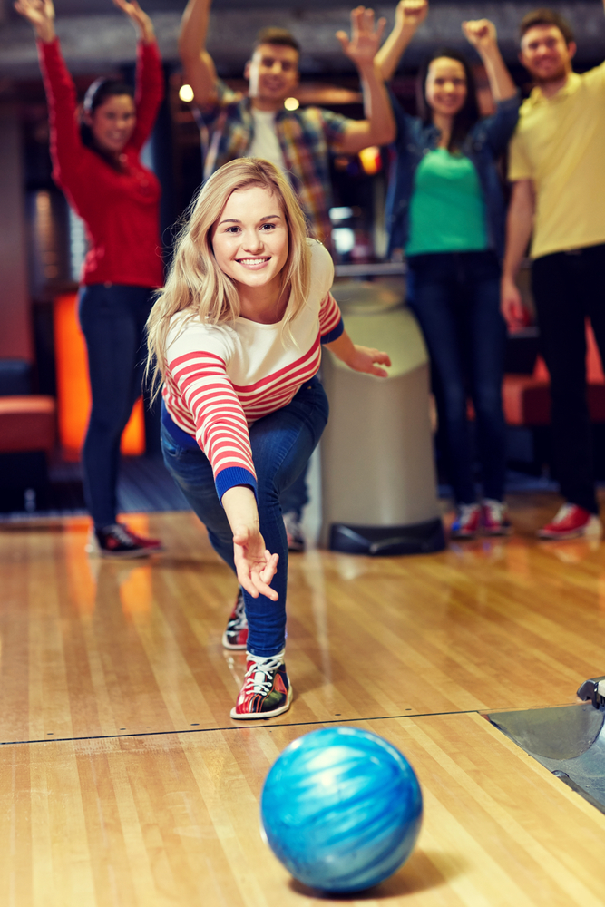 Happy young woman throwing ball in bowling club realize focus stimulates  mental alertness