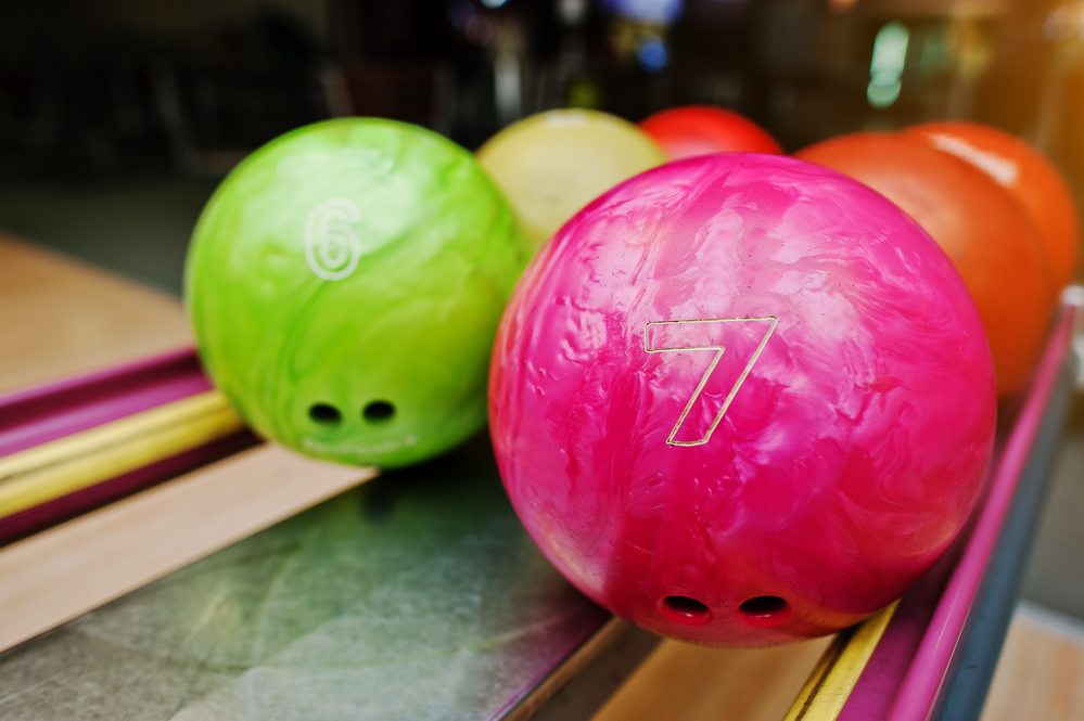 New bowling balls of various colors sitting on a ball return in a bowling alley