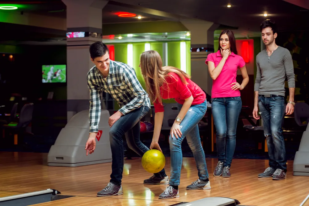 Cheerful friends at the bowling alley with the balls trying to learn how to get greater axis rotation on their roll