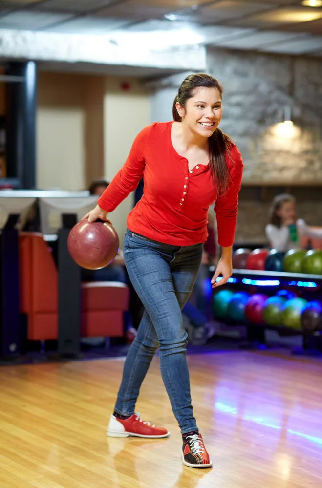 Female bowler in red shirt in bowling alley holding a red bowling ball has one shot left for a strike