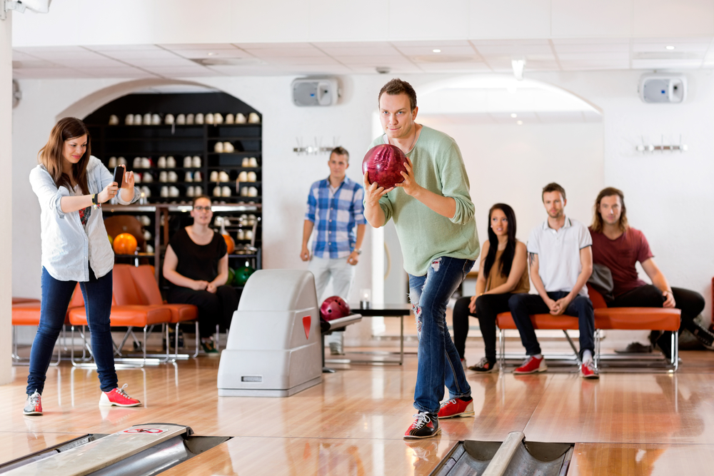 Young man bowling with female friend photographing at club after the lane man applied fresh oil