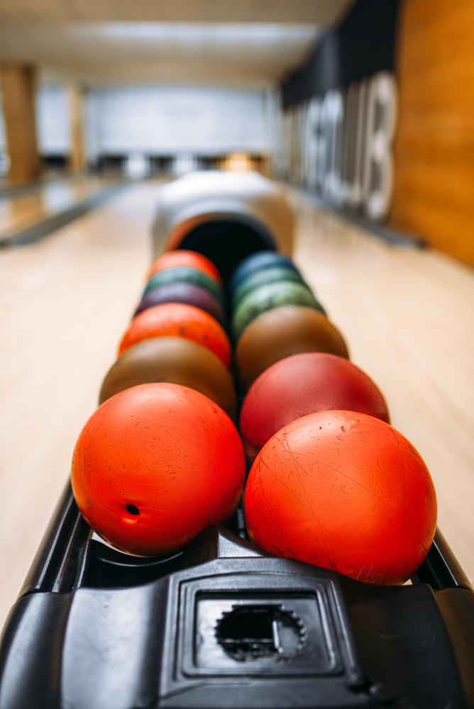 Red urethane ball in ball return on a  lane with pins in the background
