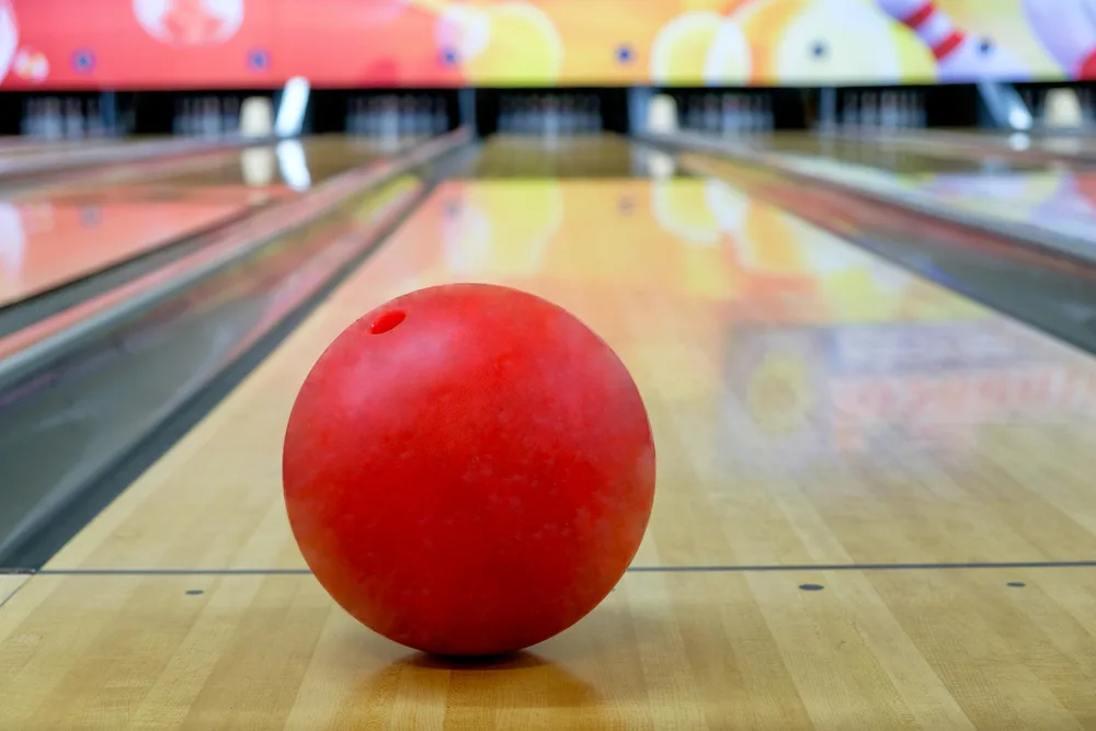 One ball sitting on bowling lane at the foul line in front of the target dots.