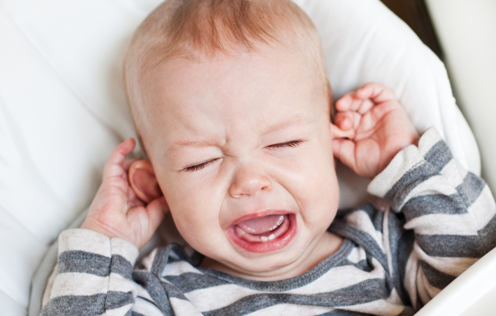 Little boy crying and holding his ear on a white background indicating the loud noise is a bother to his ears