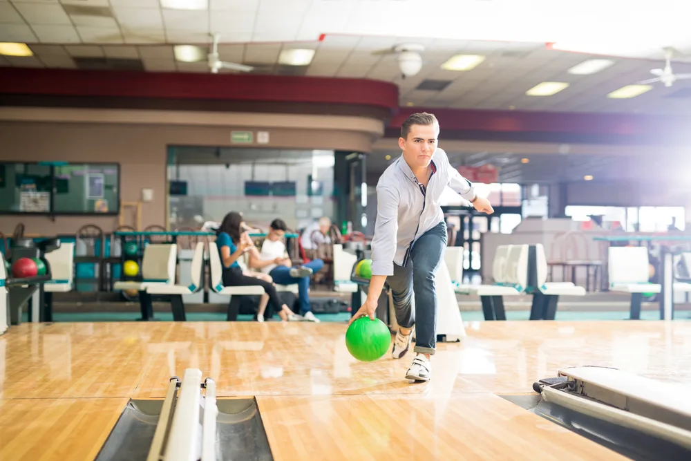 Teenage bowler playing bowling with green ball in club releases the ball as they approach the foul line