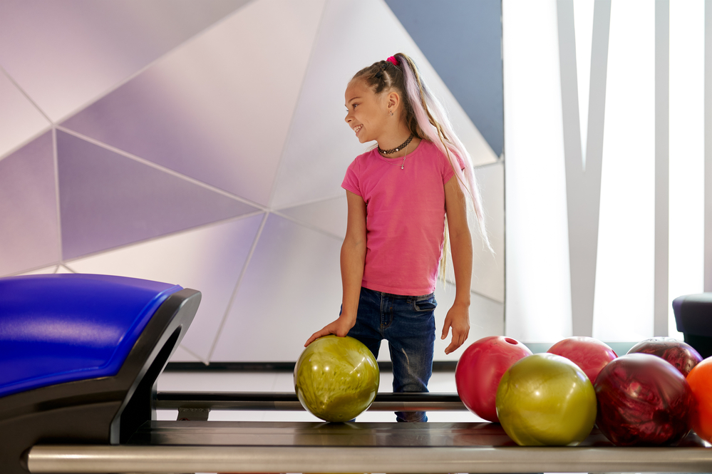 Girl holds a ball at the lane in bowling alley and because of her age, she's probably fine and not bothered by loud noise