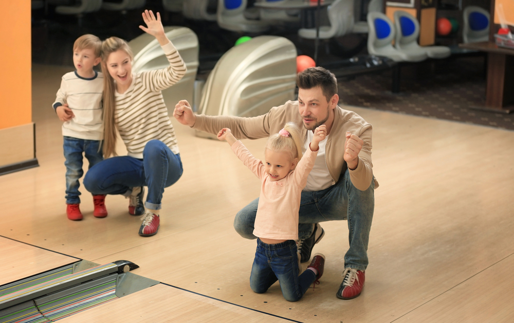 Parent and kids having family fun at a bowling alley with ball return in the back