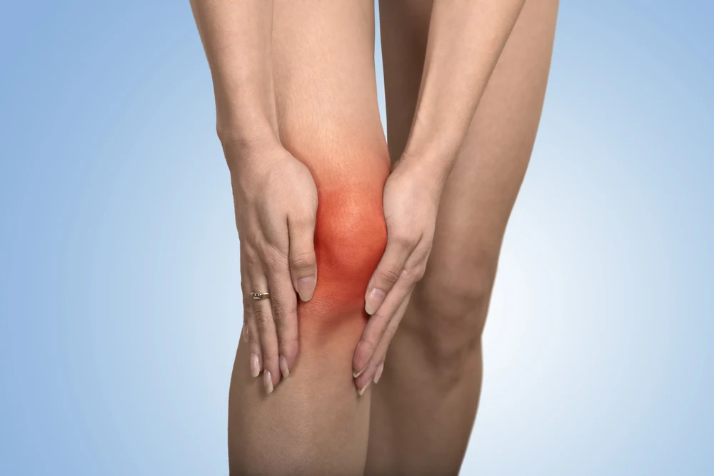 Can You Bowl With A Knee Replacement? What Activities Are Prohibited? 1 Closeup tendon knee joints problems on woman's leg indicated with knee pain indicated by red spot isolated on blue background.