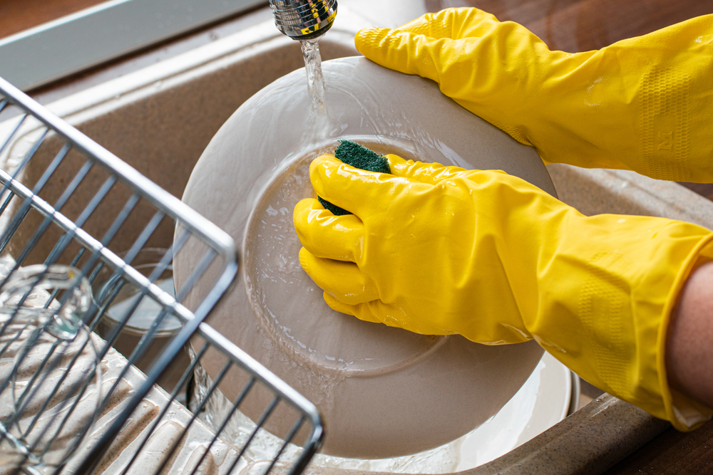 Person is washing dishes with yellow gloves is one of the best nail care tips to protect your nails