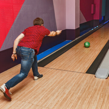 Male bowler rolling a green bowling ball