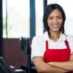 Portrait of smiling female staff standing at round 1, with arms crossed.