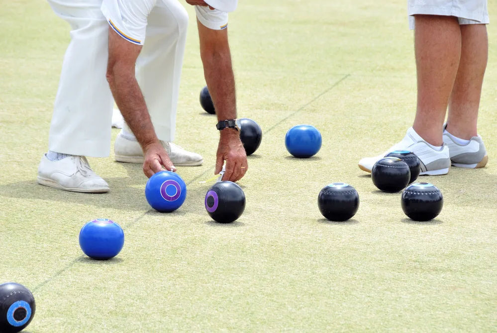 As the bowls are measured, the dark green parallel playing strips that create the rink are visible.