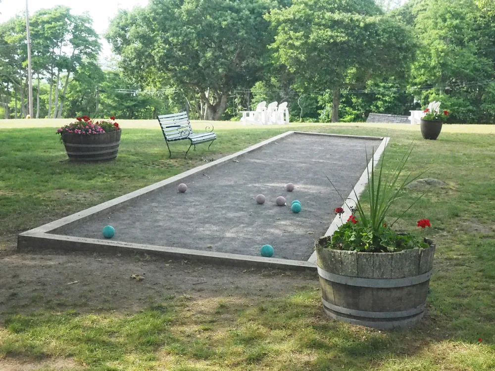 Rectangular shaped bocce ball court with a wooden border on a backyard or park next to a bench