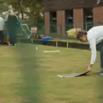 A side view shot of a woman placing a lawn bowling mat down on a bowling green, in preparation for a game.