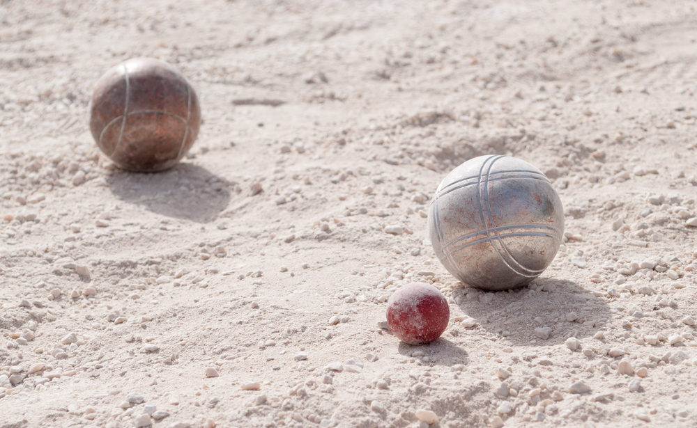 Metallic petanque balls and a small red jack on fine gravel
