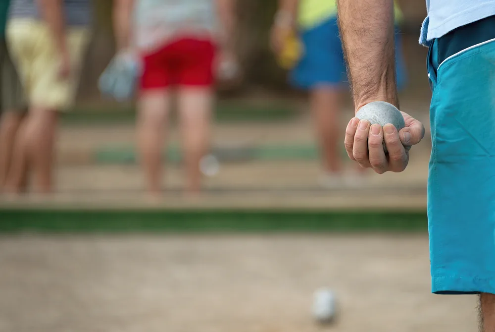 The game begins as the man in the blue shorts throws their first boule from his left hand