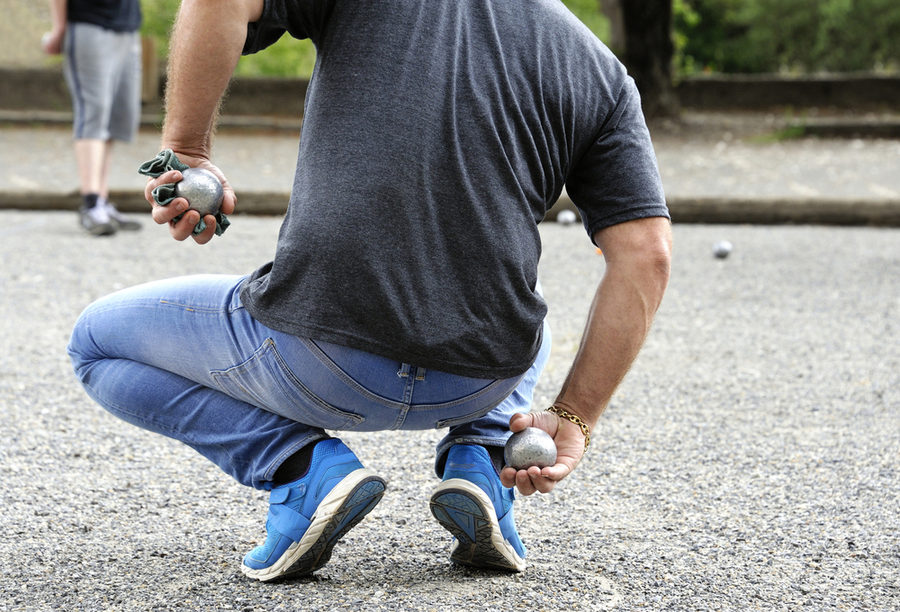 Pétanque is played in the streets of france by a man in denim pants standing in a new circle