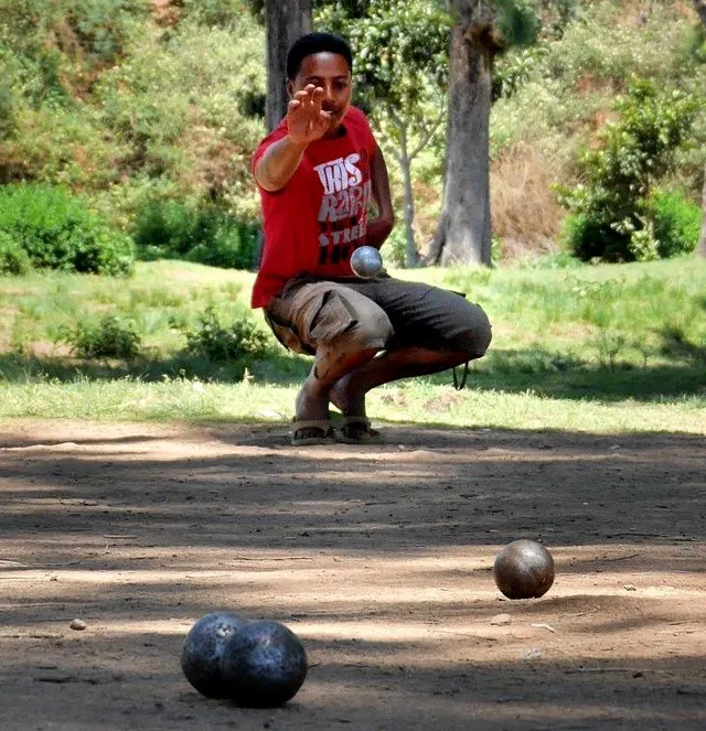 Man in france playing a round of petanque on natural terrain where he has thrown three boules