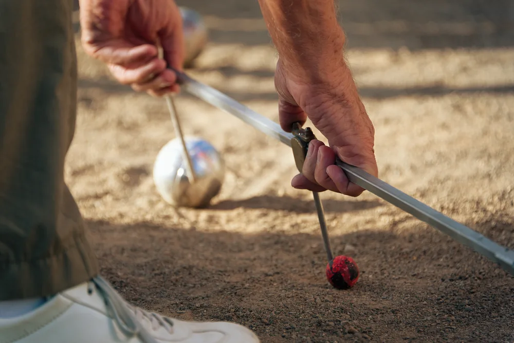 The first round of petanque is being measured with a tool to measure the distance
