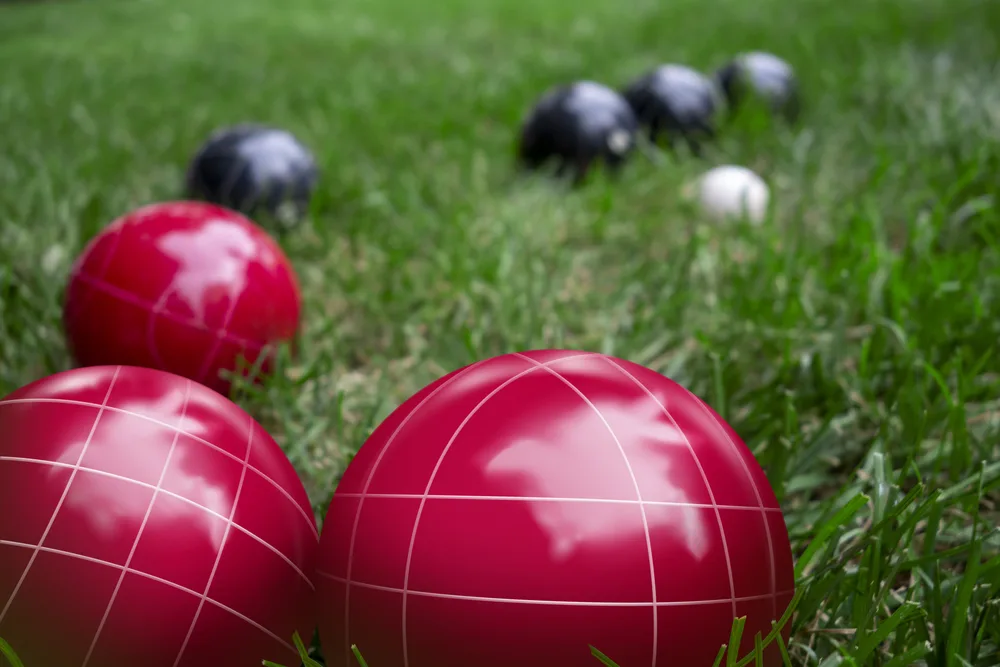 Bocce Ball Rules For Beginners: A Comprehensive Guide 1 Red and dark blue bocci balls on a green grass lawn playing the game
