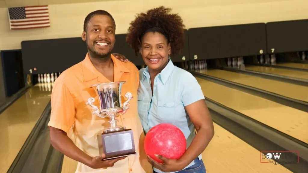 A bowling team standing in front of lanes holding a trophy and bowling ball