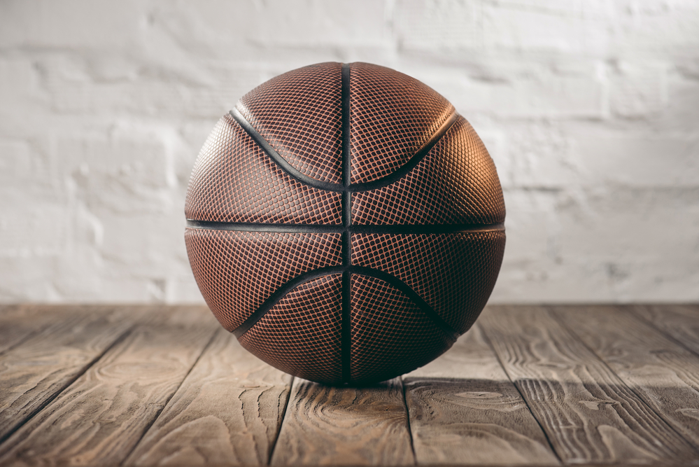 Brown basketball on hardwood floor with white brick wall in the background